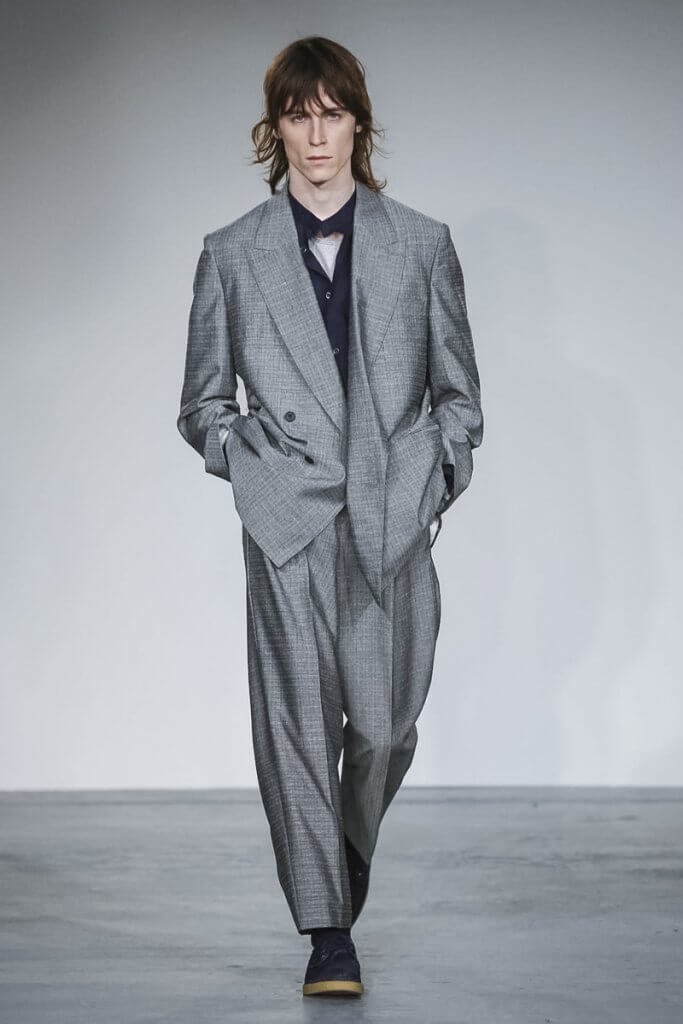 Model wearing a loose fitting silver suit on the catwalk.