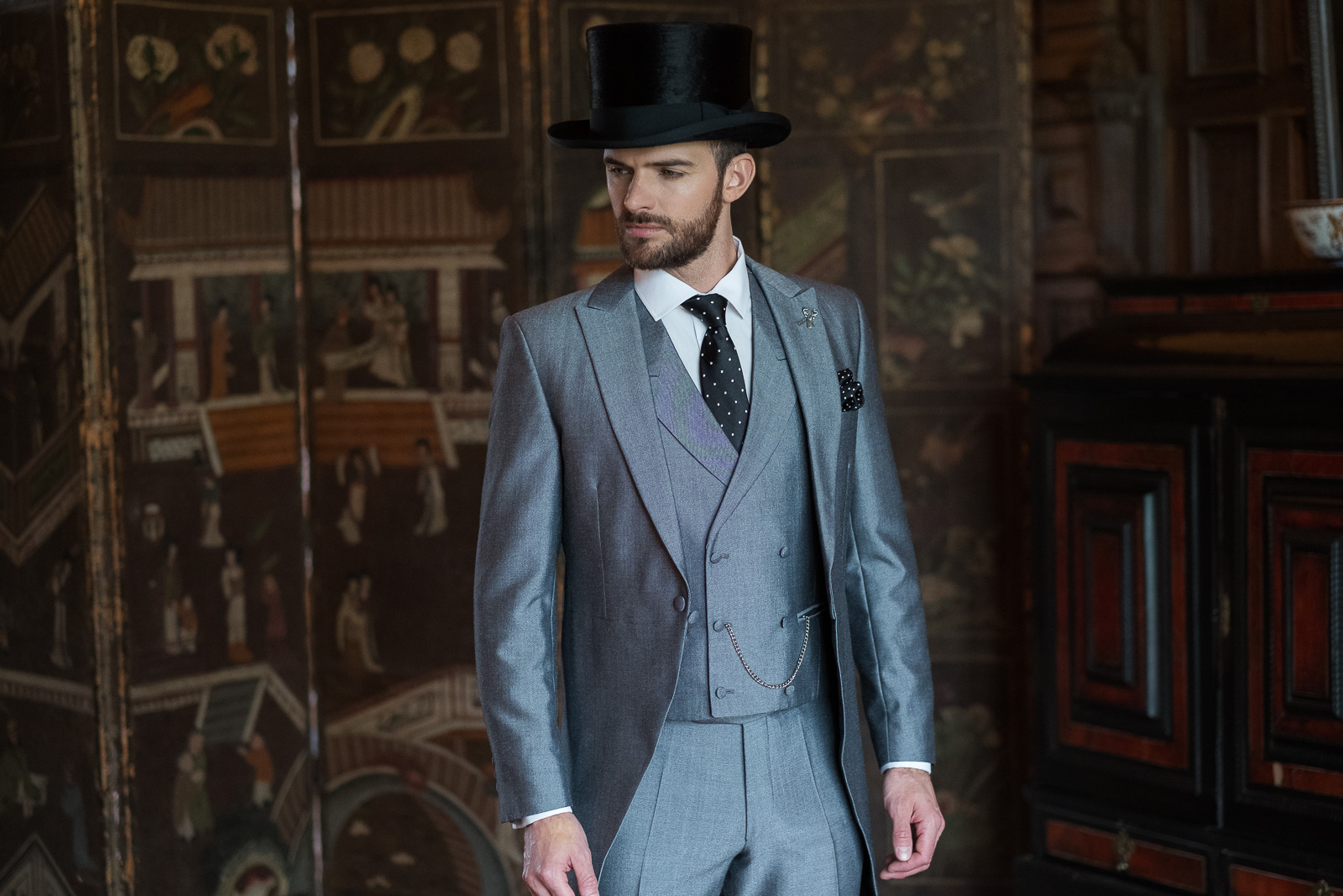 Model wears a 3 piece silver suit with a black top hat.