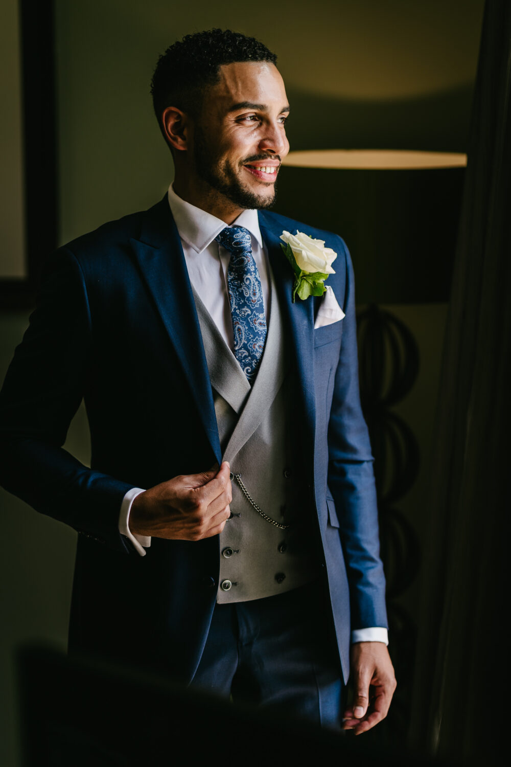 Bespoke navy suit in light weight, 100% wool. 2 piece bespoke navy suit with matching bespoke navy jacket, bespoke navy trousers and bespoke dove grey double breasted waistcoat. Features a slim fit 2 button bespoke jacket with notch lapel. Worn with bespoke white French cuff shirt and coordinating navy paisley silk tie and grey silk pocket square.
