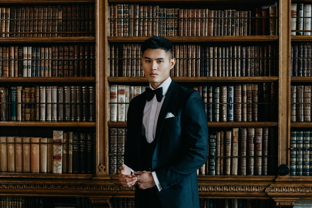Slim fit classic black dinner suit in light weight, 100% wool. 3 piece dinner suit with traditional black tux jacket, classic black dinner suit trousers and black horseshoe waistcoat. Features a slim fit 1 button black dinner jacket with classic black satin peak lapel. Worn with white studded dress shirt with French cuff shirt and large tom ford style bow tie and white pocket square.