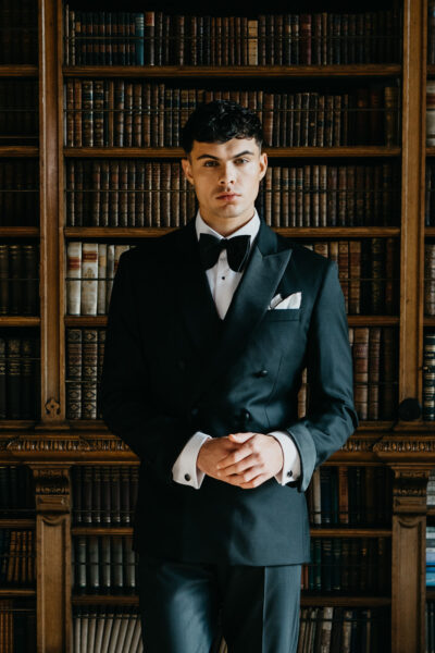 Slim fit classic black dinner suit in light weight, 100% wool. 3 piece dinner suit with traditional black tux jacket, classic black dinner suit trousers and black u shape horseshoe waistcoat. Features a slim fit 1 button black dinner jacket with classic black satin peak lapel. Worn with white studded dress shirt with French cuff shirt and large tom ford style bow tie and white pocket square.