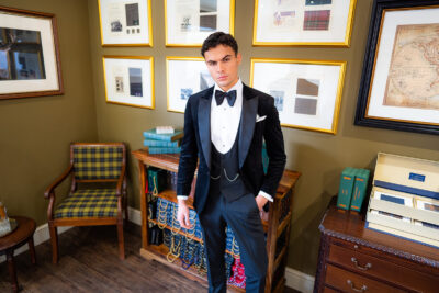 Slim fit classic black velvet dinner suit with traditional black velvet tux jacket, classic black dinner suit trousers and black u shape horseshoe waistcoat. Features a slim fit 1 button velvet dinner jacket with wide black satin peak lapel. Worn with white studded dress shirt with French cuff shirt and large tom ford style bow tie and white pocket square.