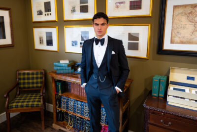 Slim fit classic black velvet dinner suit with traditional black velvet tux jacket, classic black dinner suit trousers and black V shape waistcoat. Features a slim fit 1 button velvet dinner jacket with wide black satin peak lapel. Worn with white studded dress shirt with French cuff shirt and large tom ford style bow tie and white pocket square.