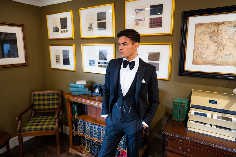 Slim fit classic black velvet dinner suit with traditional black velvet tux jacket, classic black dinner suit trousers and black V shape waistcoat. Features a slim fit 1 button velvet dinner jacket with wide black satin peak lapel. Worn with white studded dress shirt with French cuff shirt and large tom ford style bow tie and white pocket square.
