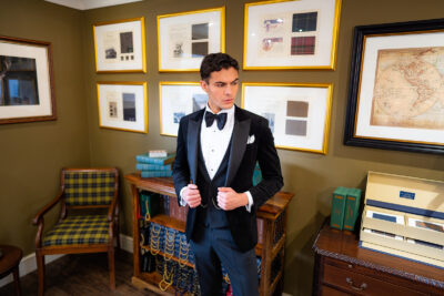 Slim fit classic black velvet dinner suit with traditional black velvet tux jacket, classic black dinner suit trousers and black low cut, V shape waistcoat. Features a slim fit 1 button velvet dinner jacket with wide black satin peak lapel. Worn with white studded dress shirt with French cuff shirt and large tom ford style bow tie and white pocket square.