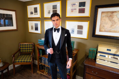 Slim fit classic black velvet dinner suit with traditional black velvet tux jacket, classic black dinner suit trousers and black low cut v shape waistcoat. Features a slim fit 1 button velvet dinner jacket with wide black satin peak lapel. Worn with white studded dress shirt with French cuff shirt and large tom ford style bow tie and white pocket square.