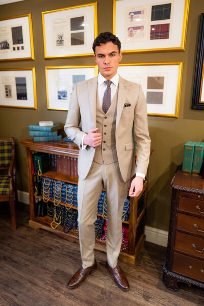 Slim fit beige suit in light weight, 100% wool. 3 piece beige suit with matching beige jacket, beige single breasted waistcoat and beige trousers. Features a slim fit 2 button jacket with classic notch lapel. Worn with white French cuff shirt and coordinating tonal brown silk tie and pocket square