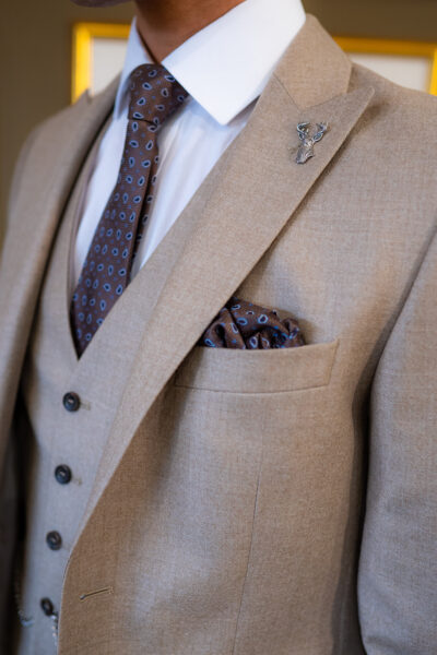 Slim fit beige custom suit in light weight, 100% wool. 3 piece beige custom suit with matching beige jacket, beige single breasted waistcoat and beige trousers. Features a slim fit 2 button jacket with classic notch lapel. Worn with white French cuff shirt and coordinating tonal brown silk tie and pocket square.