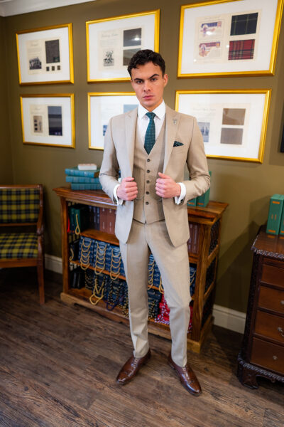 Slim fit beige suit in light weight, 100% wool. 3 piece beige suit with matching beige jacket, beige single breasted waistcoat and beige trousers. Features a slim fit 2 button jacket with classic notch lapel. Worn with white French cuff shirt and coordinating green spot silk tie and pocket square.