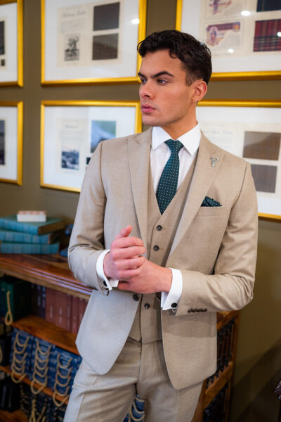 Slim fit beige suit in light weight, 100% wool. 3 piece beige suit with matching beige jacket, beige single breasted waistcoat and beige trousers. Features a slim fit 2 button jacket with classic notch lapel. Worn with white French cuff shirt and coordinating green spot silk tie and pocket square.