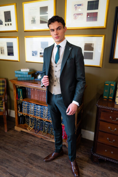 Slim fit green custom suit in light weight, 100% wool. 3 piece green custom suit with matching green jacket, green trousers and contrast beige single breasted waistcoat. Features a slim fit 2 button jacket with classic notch lapel. Worn with white French cuff shirt and green and white spot silk tie and pocket square.