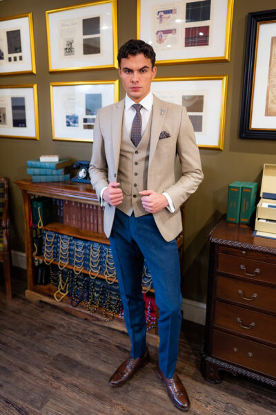 Slim fit beige suit in light weight, 100% wool. 3 piece beige suit with matching beige jacket, beige single breasted waistcoat and contrast blue trousers. Features a slim fit 2 button jacket with classic notch lapel. Worn with white French cuff shirt and coordinating blue paisley silk tie and pocket square.