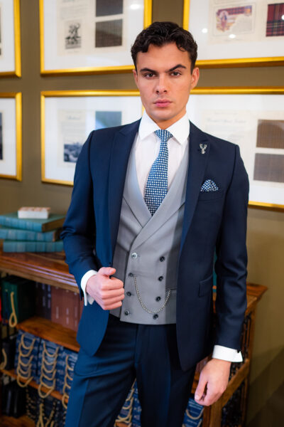 Slim fit navy suit in light weight, 100% wool. 3 piece navy suit with matching navy jacket, navy trousers and classic dove grey double breasted waistcoat. Features a slim fit 1 button jacket with classic peak lapel. Worn with white French cuff shirt and coordinating navy and white silk tie and pocket square.