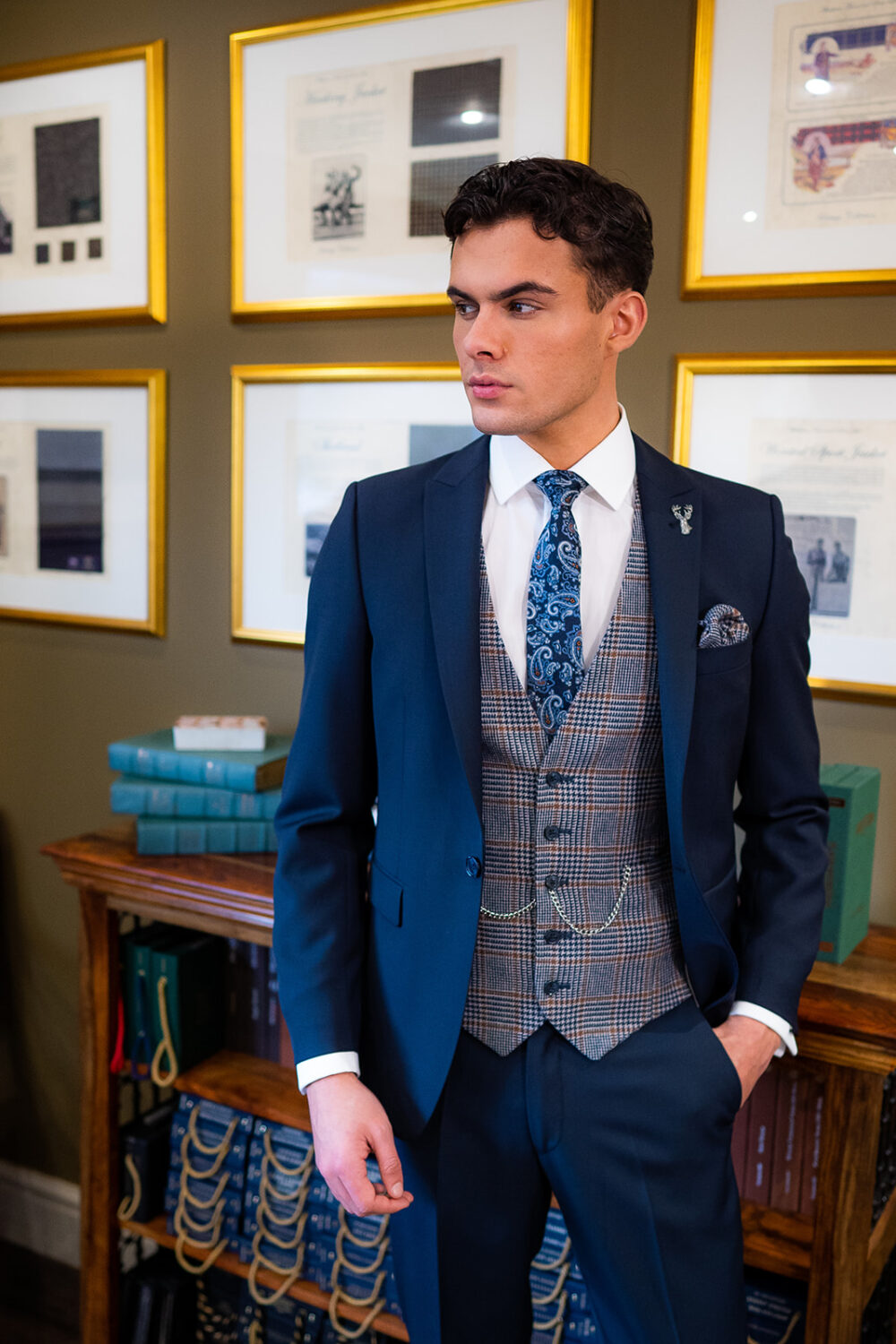 Slim fit navy suit in light weight, 100% wool. 3 piece navy suit with matching navy jacket, navy trousers and contrast blue and brown tweed waistcoat. Features a slim fit 1 button jacket with classic peak lapel. Worn with white French cuff shirt and coordinating blue silk tie and blue and brown tweed pocket square.