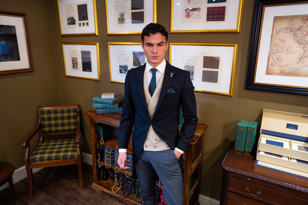 Slim fit classic black morning suit in light weight, 100% wool. 3 piece morning suit with traditional black morning jacket, classic stripe trousers and traditional beige, peak lapel double breasted waistcoat. Features a slim fit 1 button morning jacket with classic peak lapel. Worn with white French cuff shirt and coordinating green and white silk tie and pocket square.